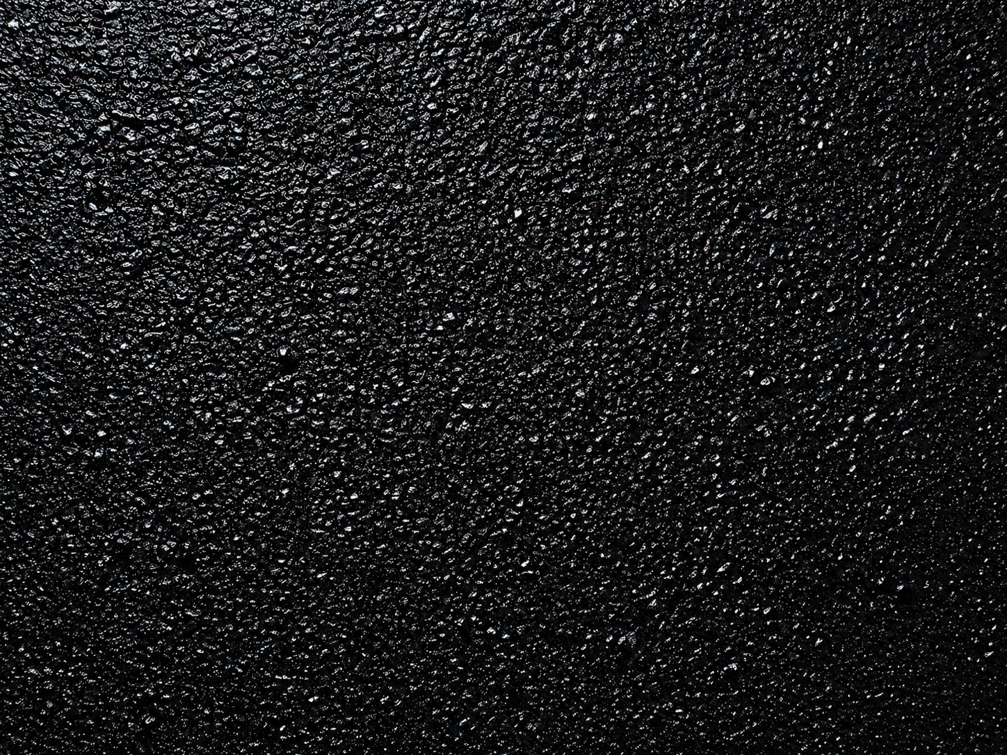 Macro close-up of freshly sealcoated asphalt — glossy jet-black grain catching subtle light